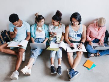 Overhead portrait of international students waiting for test in college. Group of university mates sitting on the floor with books and laptops, doing homework.